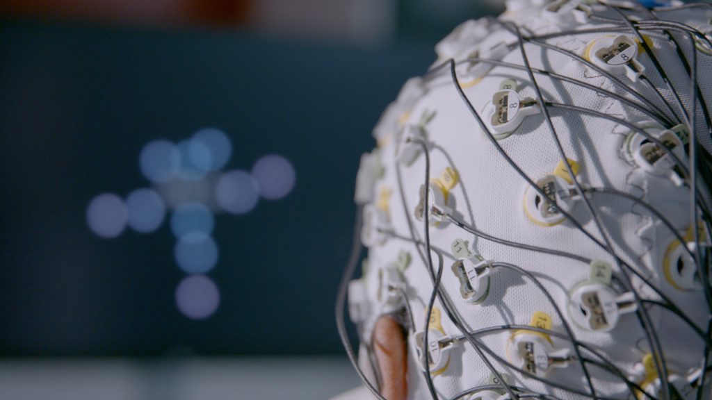 Ein Experiment zu passiven Gehirn-Computer-Schnittstellen/Passive BCIs. Auf der Kopfhaut aufliegende Elektroden zeichnen die Gehirnaktivität auf und übersetzen diese in Echtzeit in Veränderungen, die auf dem Computerbildschirm sichtbar sind. 
Foto: Copyright „Gedachtegoed“