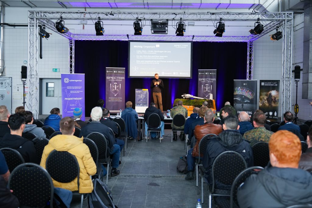 Dr. Julian Laufs, Projektleiter der SPECTRA Challenge von der Cyberagentur, eröffnete die Pitch Days auf dem Fliegerhorst in Erding vor Jury und Teilnehmenden aus Wissenschaft, Wirtschaft und Startups. Foto: CIHBw