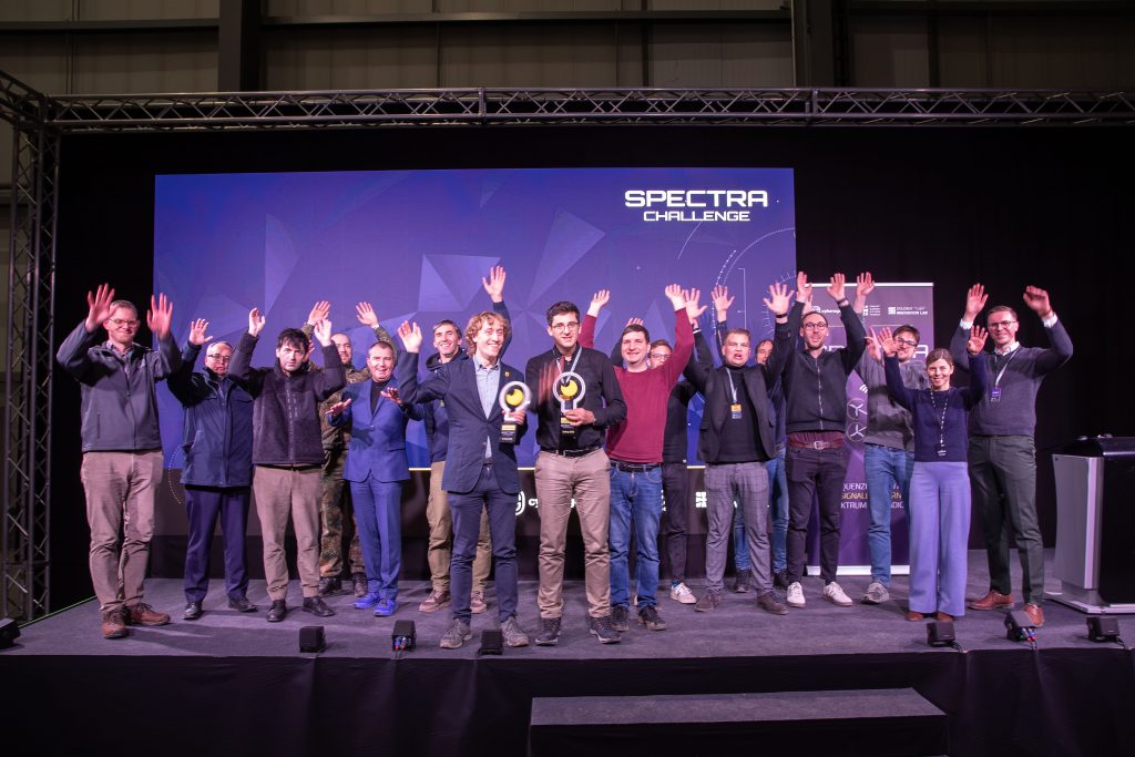 Conclusion of the SPECTRA Challenge in Erding: The winning teams of the practical and moonshot tracks and representatives of the three cooperating innovation units celebrate together on stage.